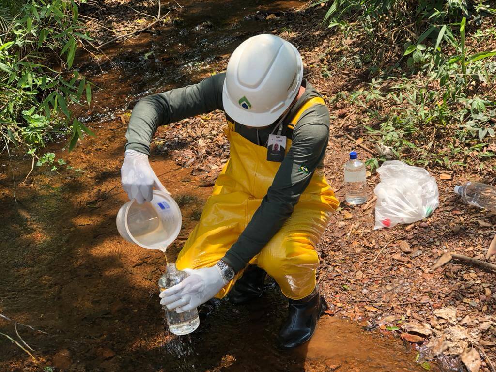 Profissional com fato impermeável da Ambsolution realiza recolha de amostra em riacho para amostragem de águas superficiais em campo