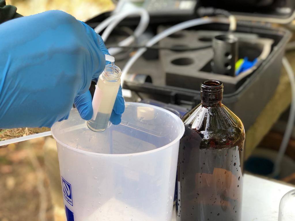 Mão com luva realiza acondicionamento de amostra líquida para análise química e classificação no gerenciamento de resíduos da Ambsolution