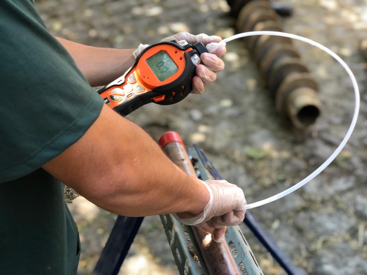 Técnico com luvas opera detector PID de gases em amostragem de campo para estudo de avaliação de risco à saúde humana da Ambsolution
