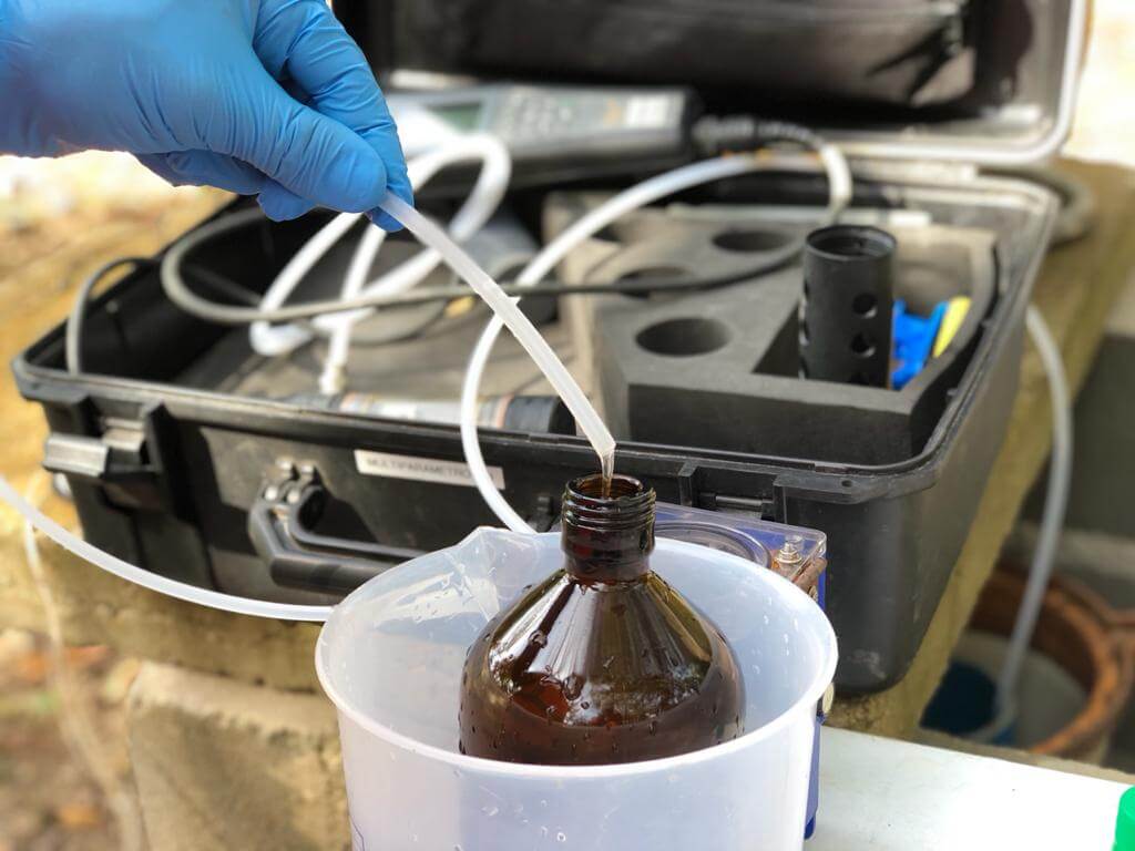 Profissional da Ambsolution Engenharia Ambiental coleta amostra líquida em campo para estudos de avaliação ambiental preliminar