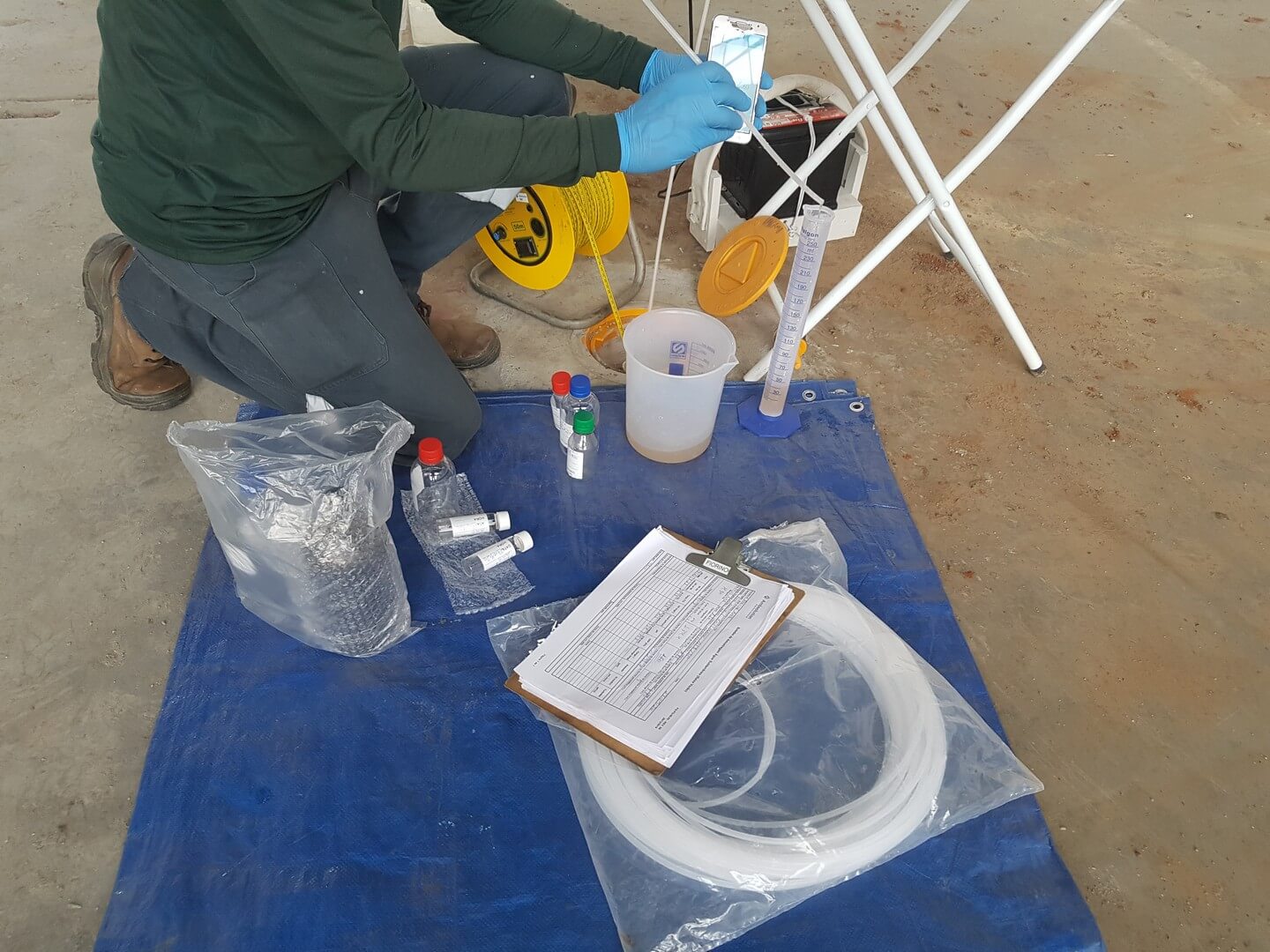 Técnico com luvas organiza frascos e equipamentos de coleta em campo para laudos de caracterização de resíduos da Ambsolution