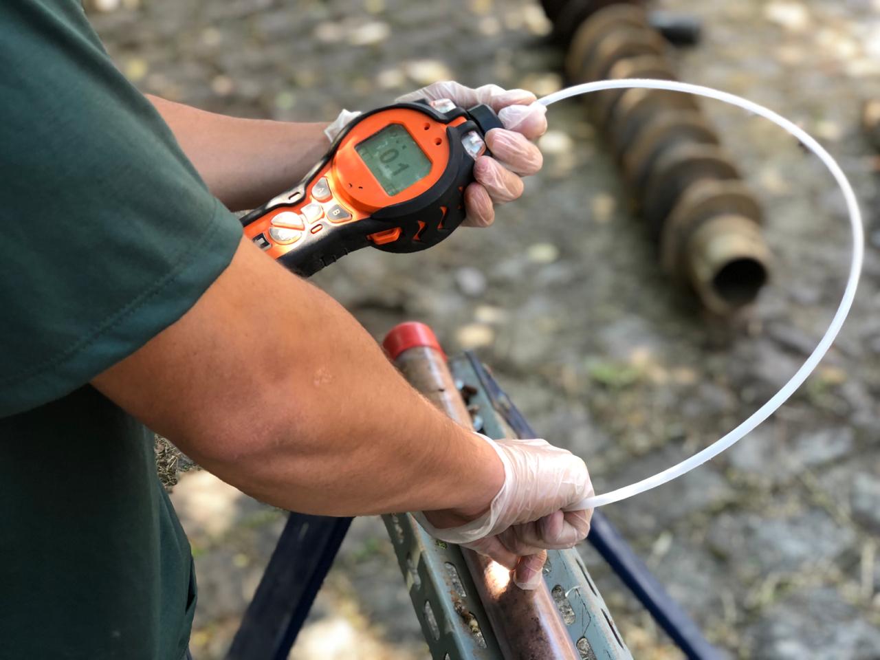 Profissional com luvas opera detector portátil PID para triagem de gases em campo no monitoramento ambiental da Ambsolution